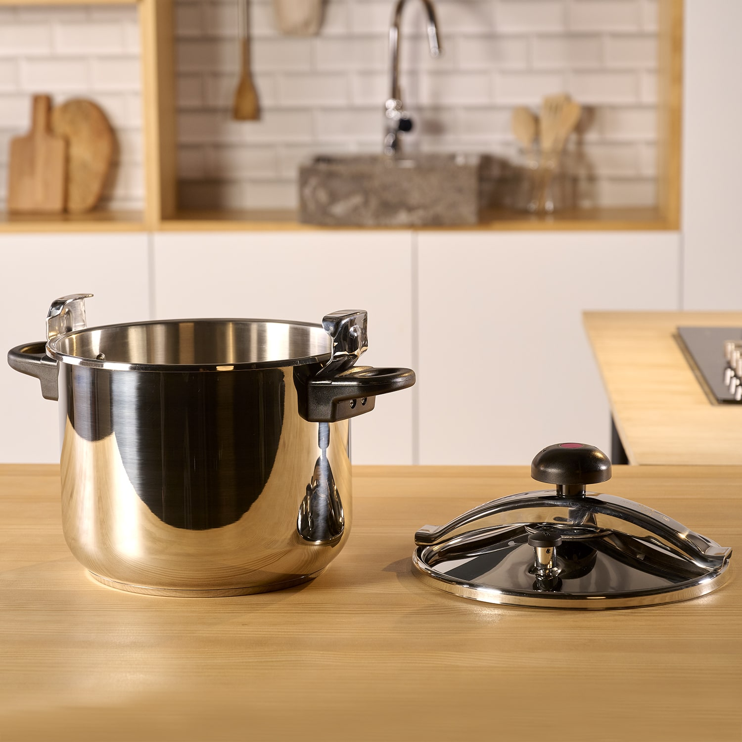 Una olla a presión de acero inoxidable con tapa abierta sobre una superficie de madera. El fondo es una cocina.