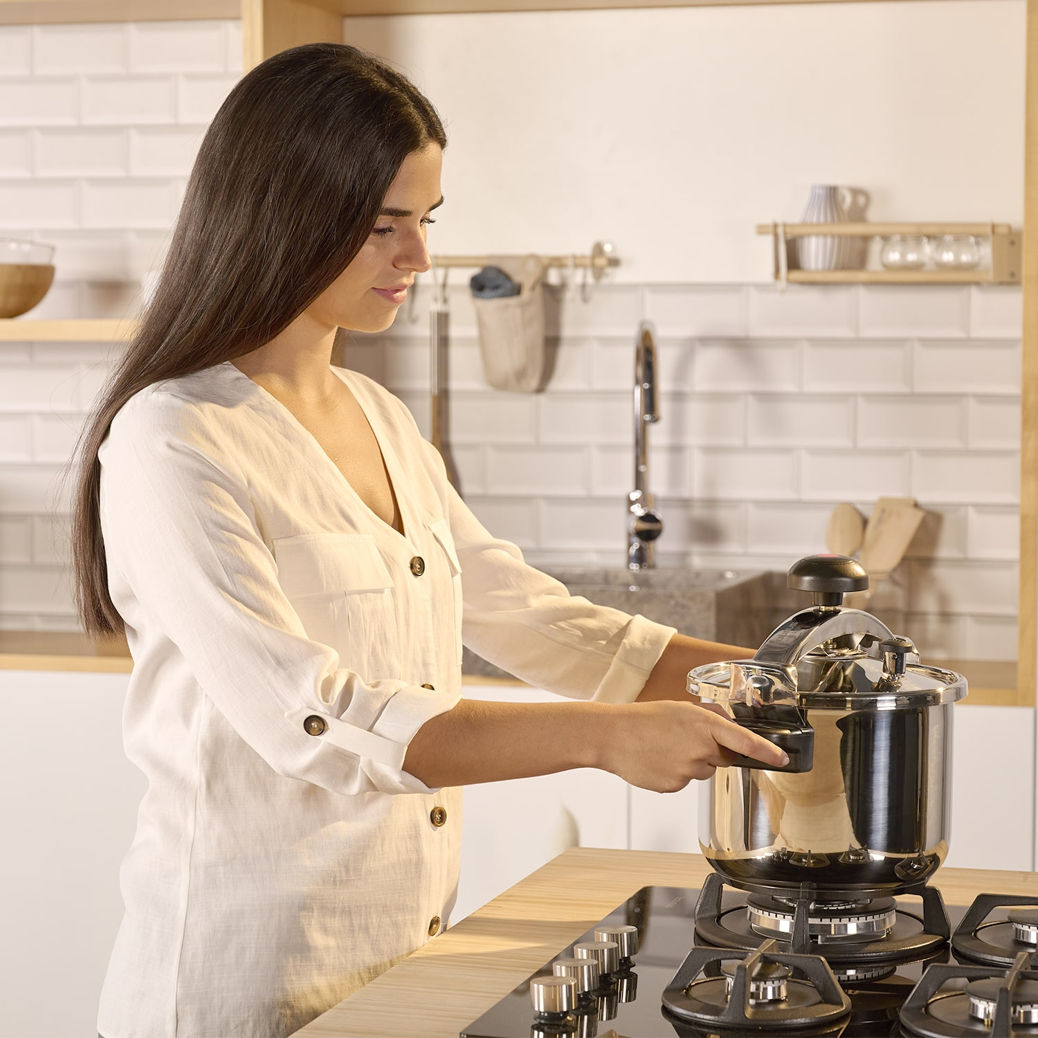 Mujer con camisa blanca preparando comida en una estufa con una olla a presión.