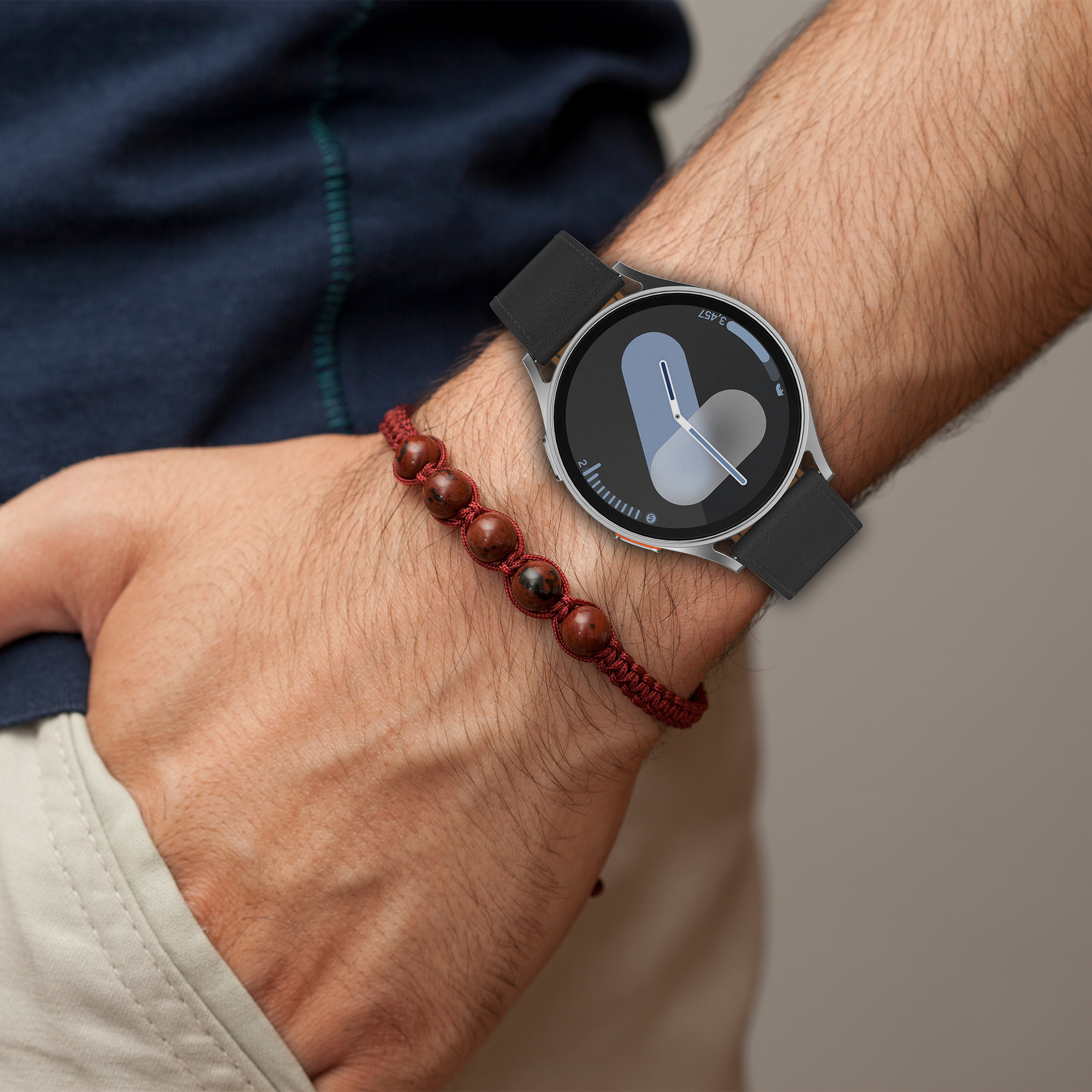 Person trägt Uhr und Armband. Uhr hat schwarzes Armband und silbernes Gehäuse.