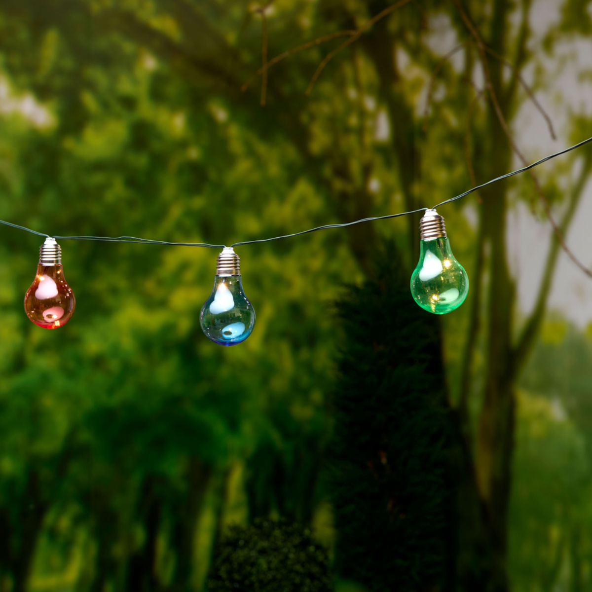 Trois ampoules colorées suspendues à un fil dans un jardin.