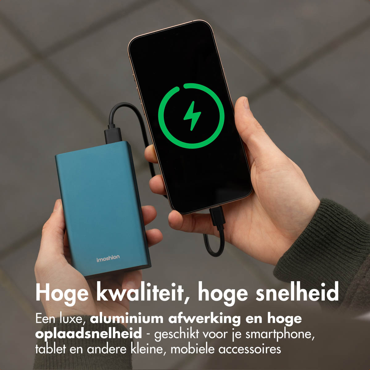Une personne tenant une batterie externe bleue chargeant un smartphone noir, avec une icône d'éclair sur l'écran.