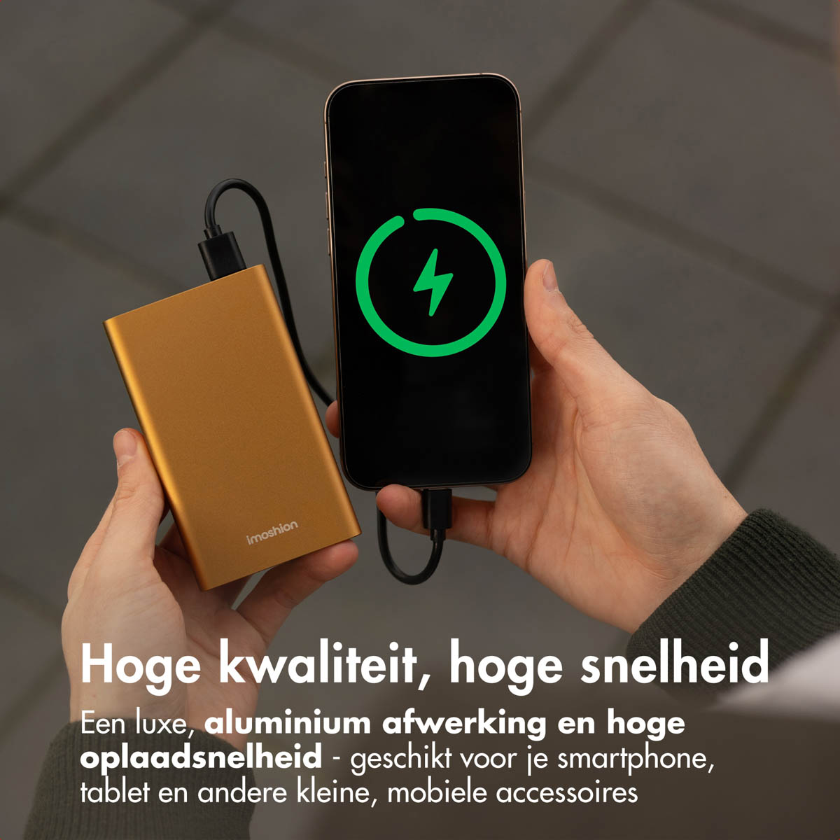 Une main tenant une batterie externe dorée à côté d'un téléphone. Le téléphone se charge, affichant une icône de foudre.