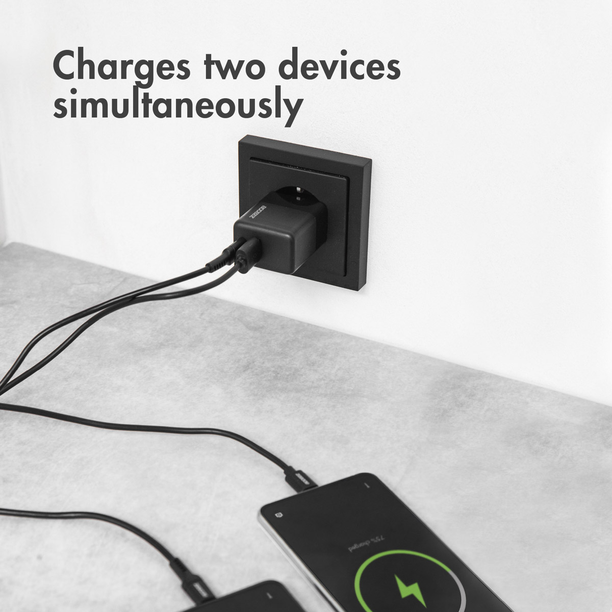 Un chargeur noir dans une prise murale. Un téléphone est en charge.