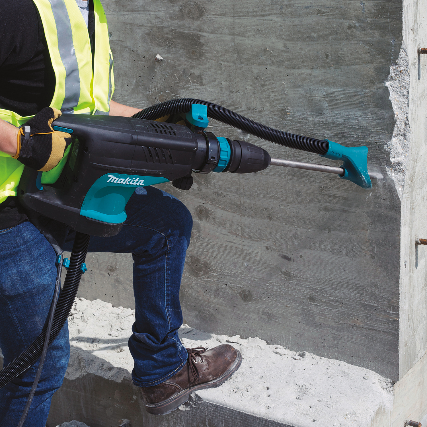 Persona che utilizza un trapano Makita su un muro di cemento. Indossa un giubbotto di sicurezza.