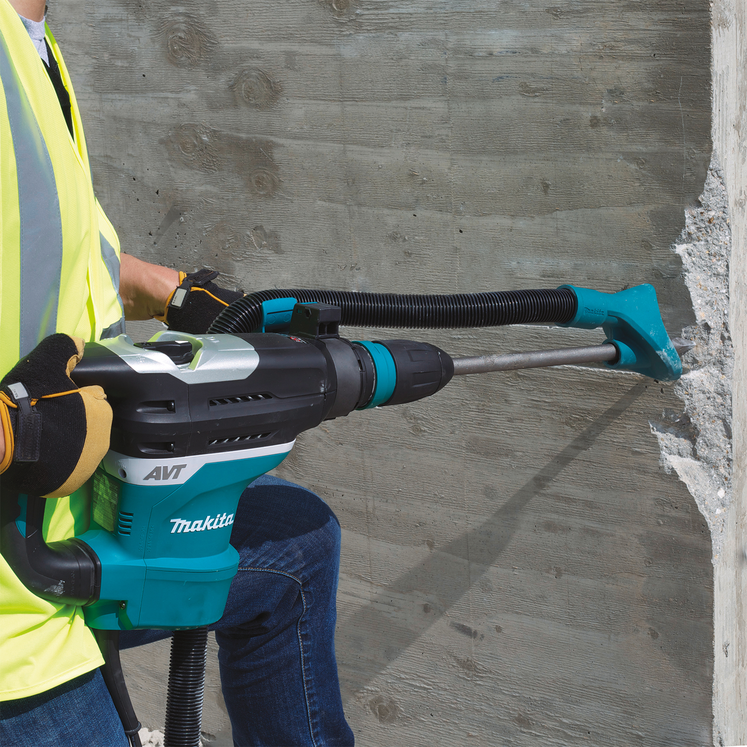 Persona con giubbotto di sicurezza usa un martello pneumatico Makita per rompere un muro di cemento.