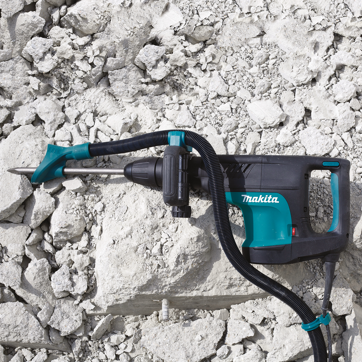 Trapano a percussione Makita su roccia bianca. Schema di colori nero e verde acqua. Tubo collegato.