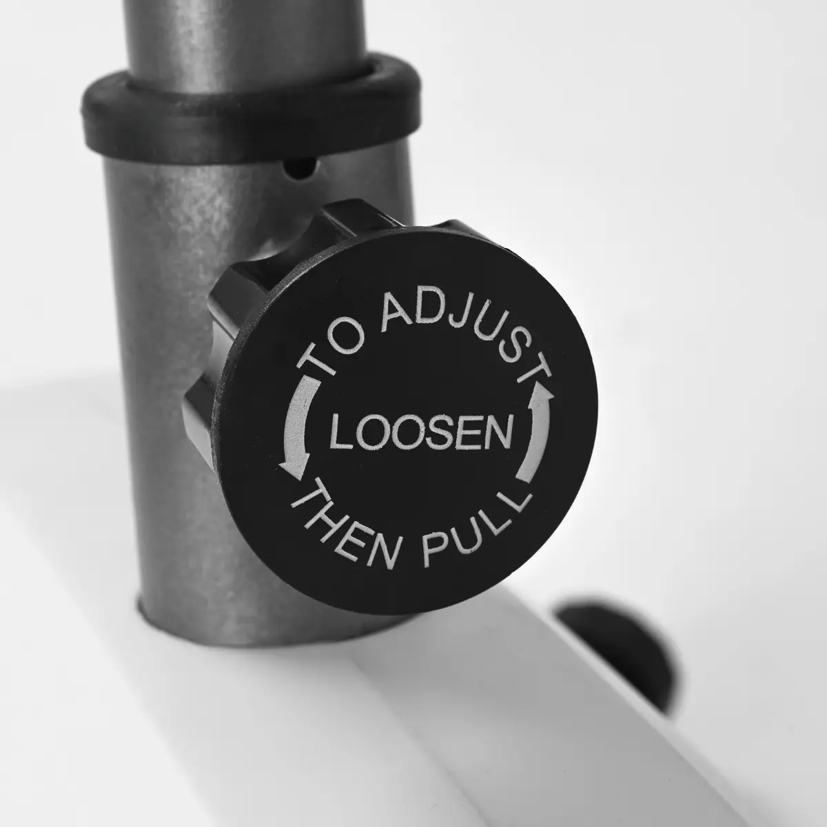 Close-up van een zwarte knop op een machine. Tekst zegt 'To Adjust, Loosen Then Pull'.