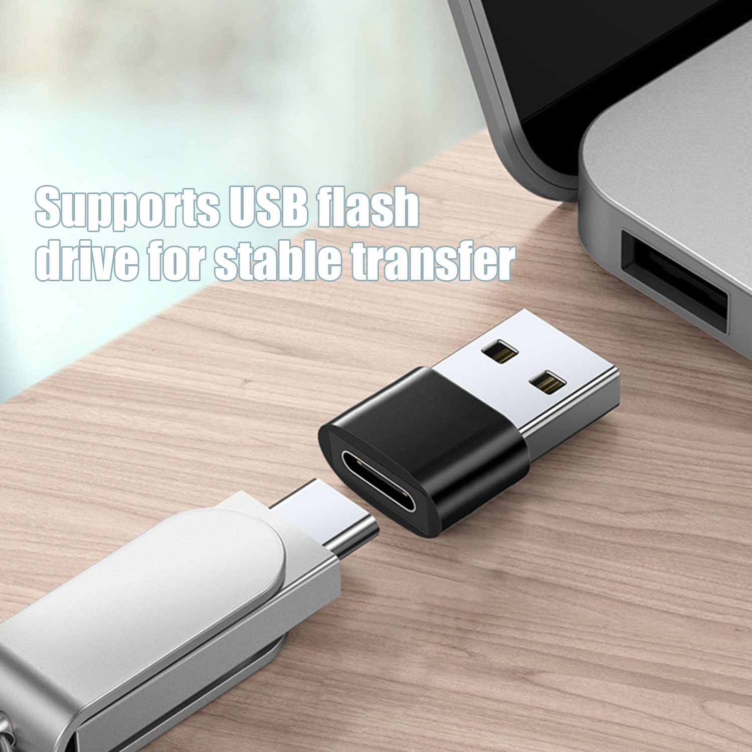 Adapter USB-C obok pendrive'a USB i laptopa. Adapter jest czarny i srebrny. Pendrive jest srebrny.