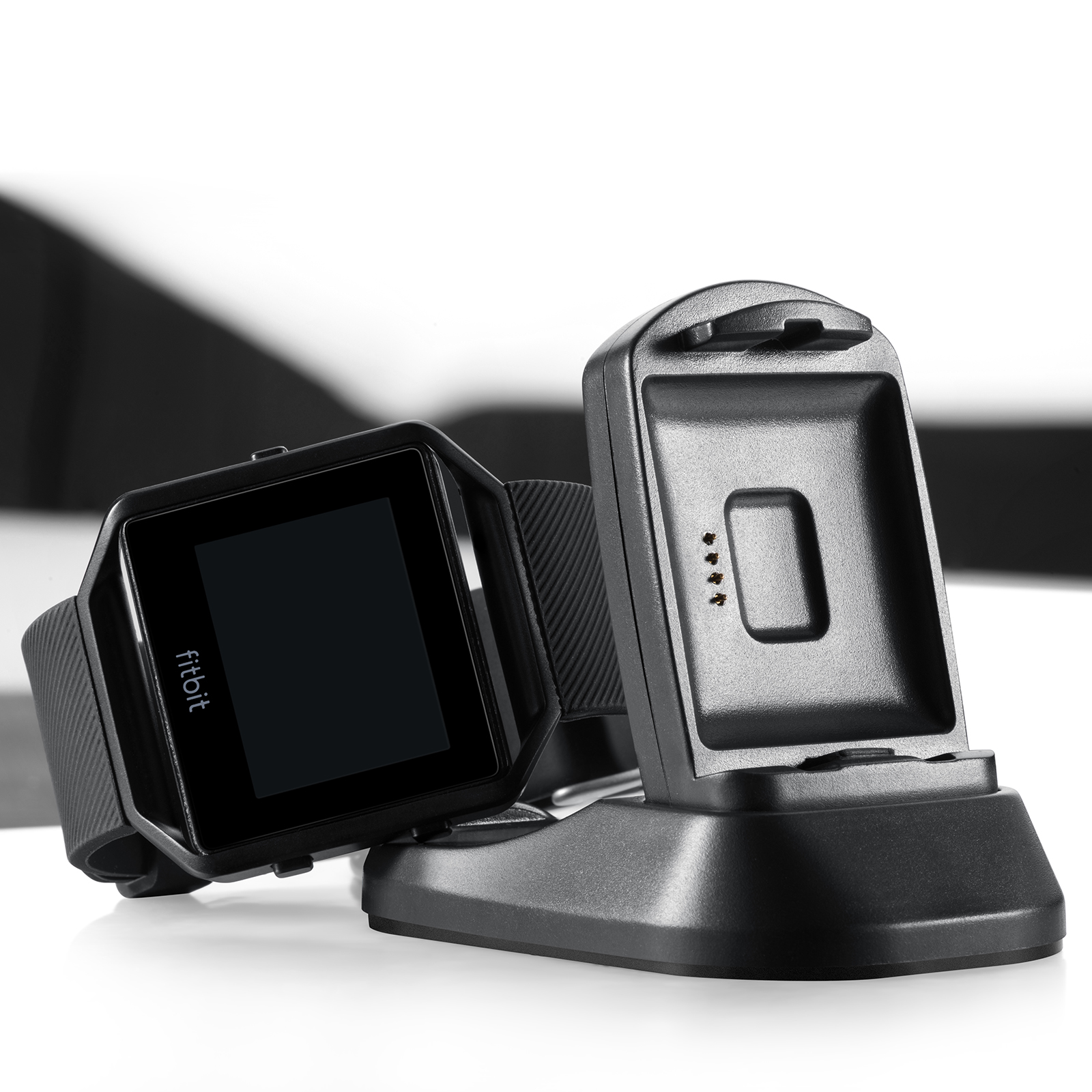 Schwarze Fitbit Smartwatch und Ladestation auf weißer Oberfläche. Die Uhr ist schwarz.