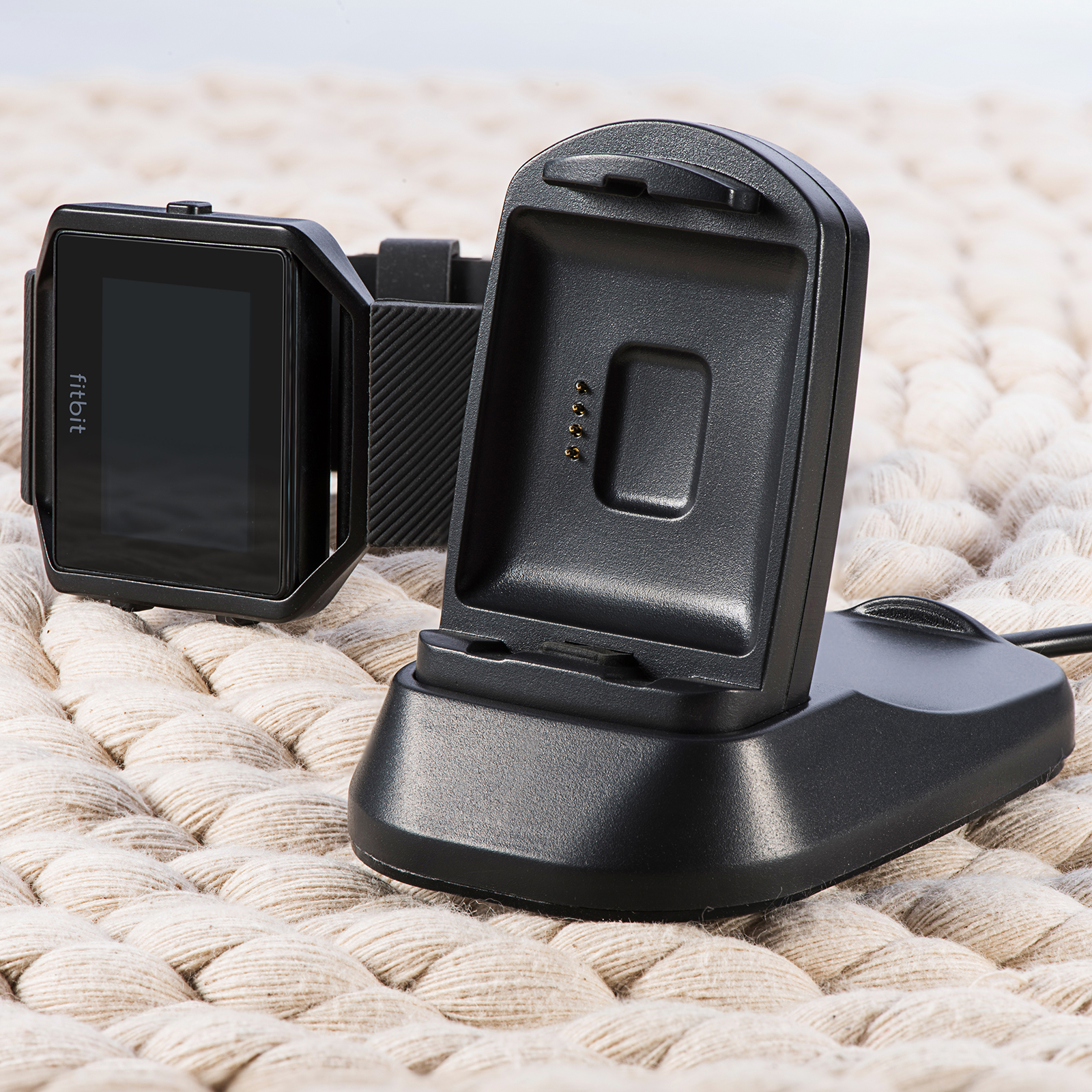 Schwarze Fitbit-Uhr auf weißer Strickoberfläche, mit Ladestation.