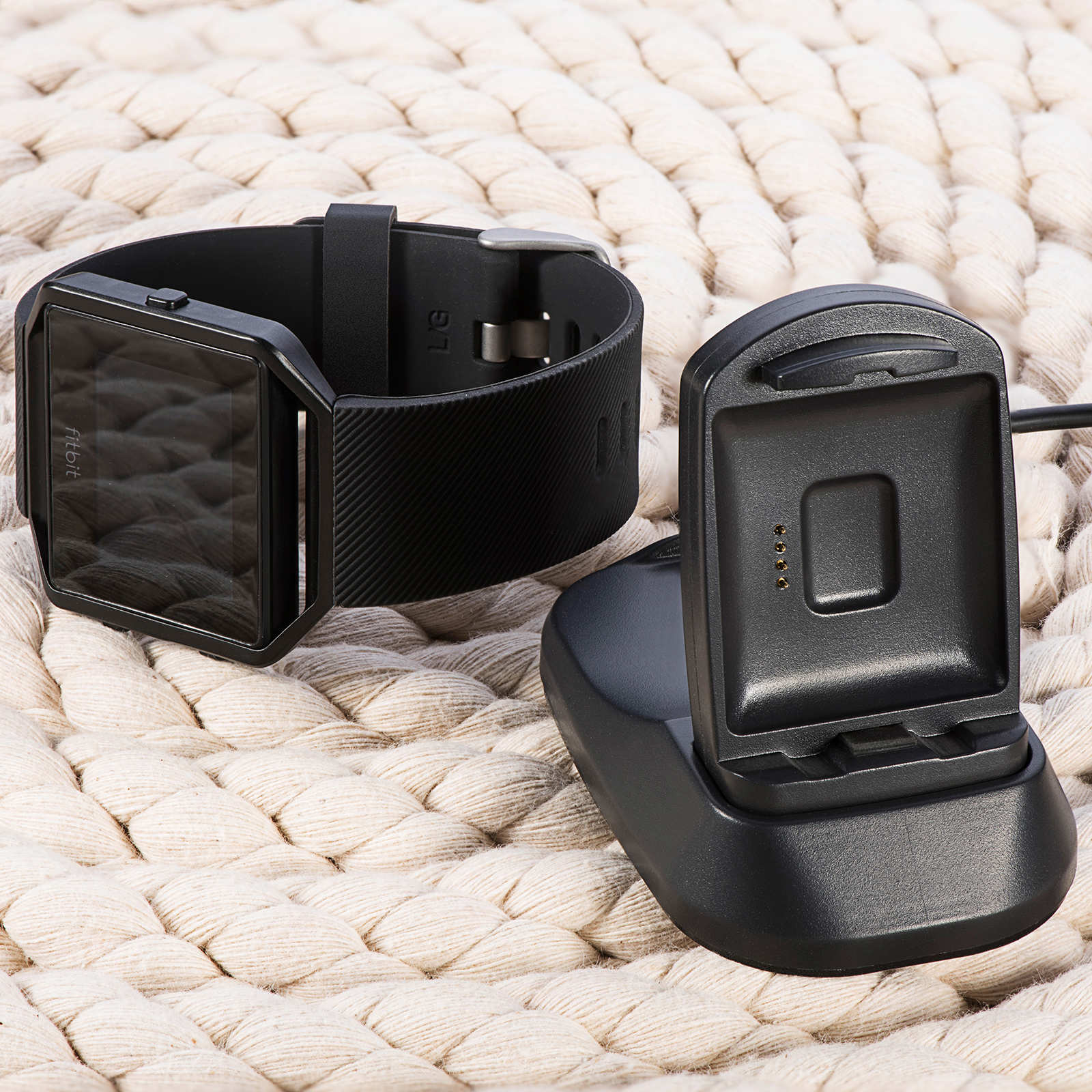 Eine schwarze Fitbit-Uhr auf einer weißen, gewebten Oberfläche mit ihrer schwarzen Ladestation.