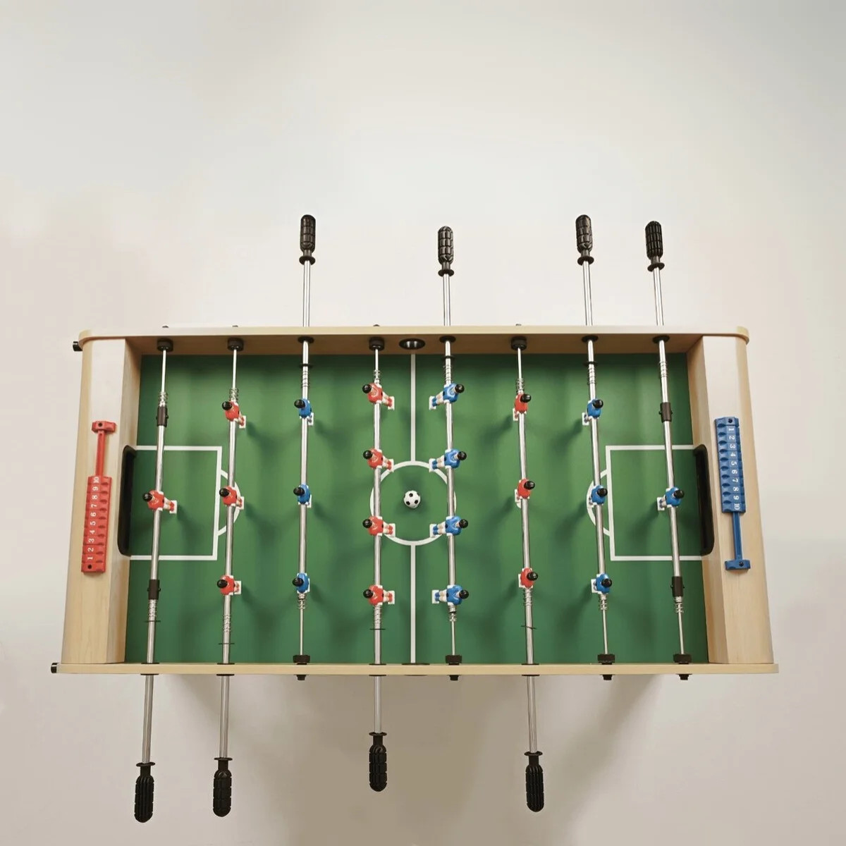 Foosball table, top view. Green field with white lines, red and blue players, and a white ball.
