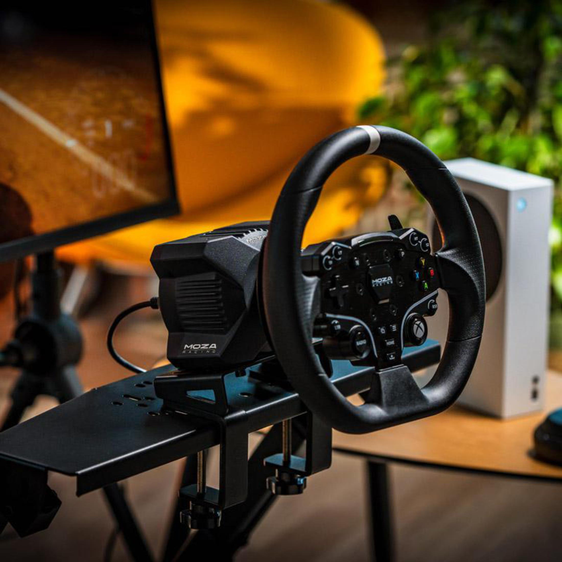 Volant noir, monté sur un support. Derrière, une Xbox Series S blanche et un moniteur.