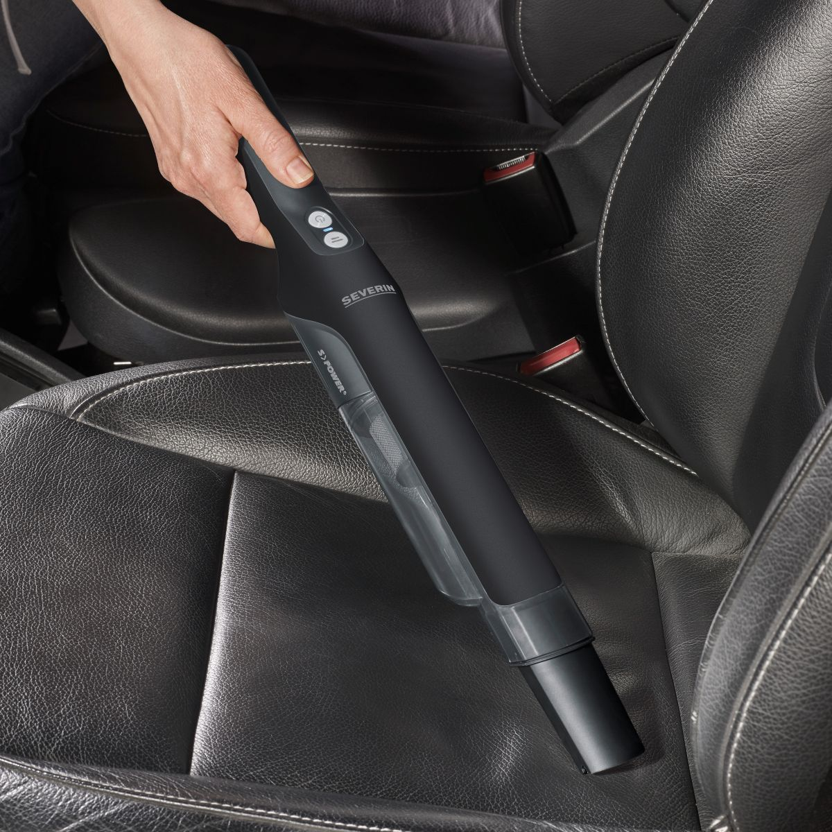Une main utilise un aspirateur Severin noir à l'intérieur d'une voiture sur un siège en cuir noir.