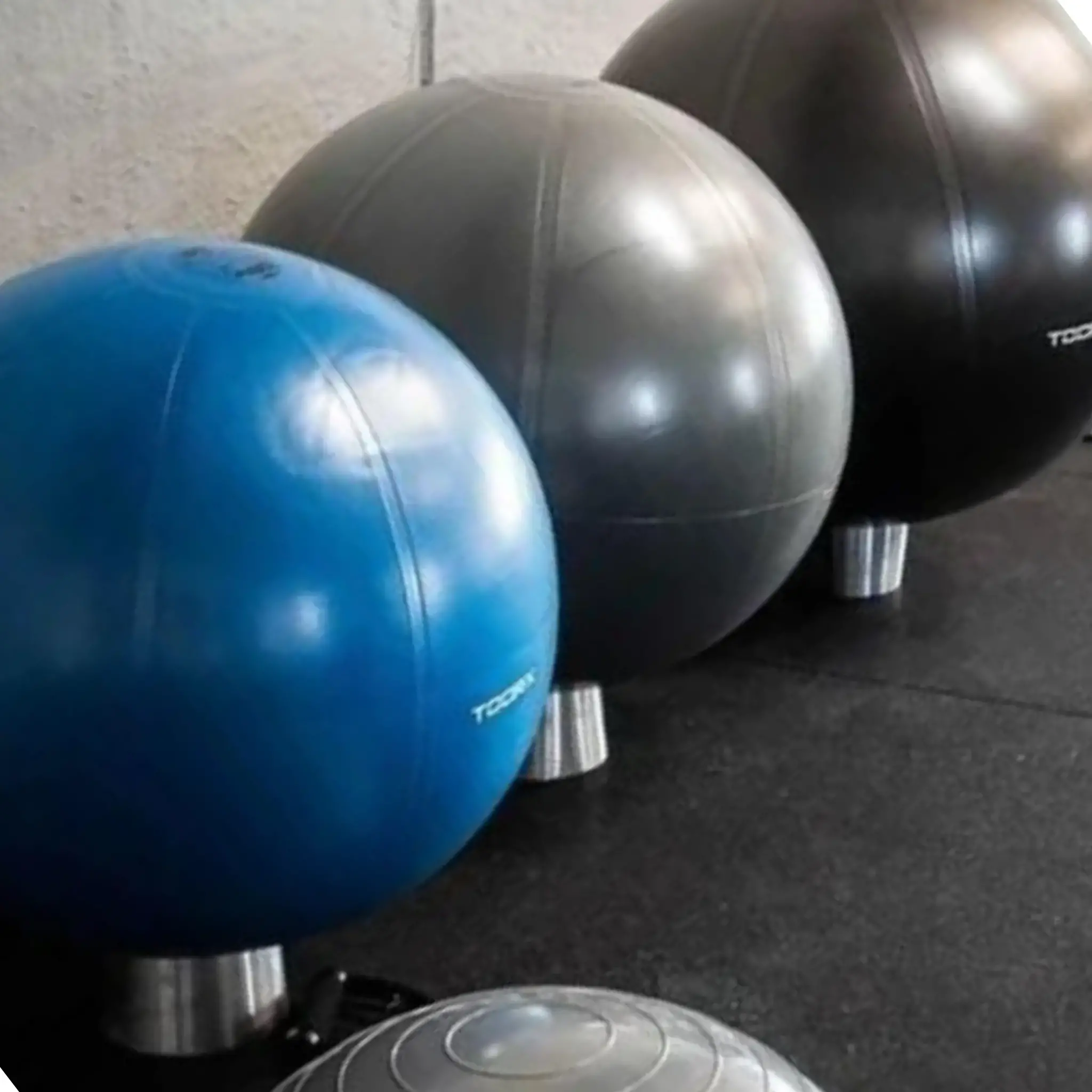 Drie fitnessballen, blauw, grijs en zwart, op een zwarte vloer.