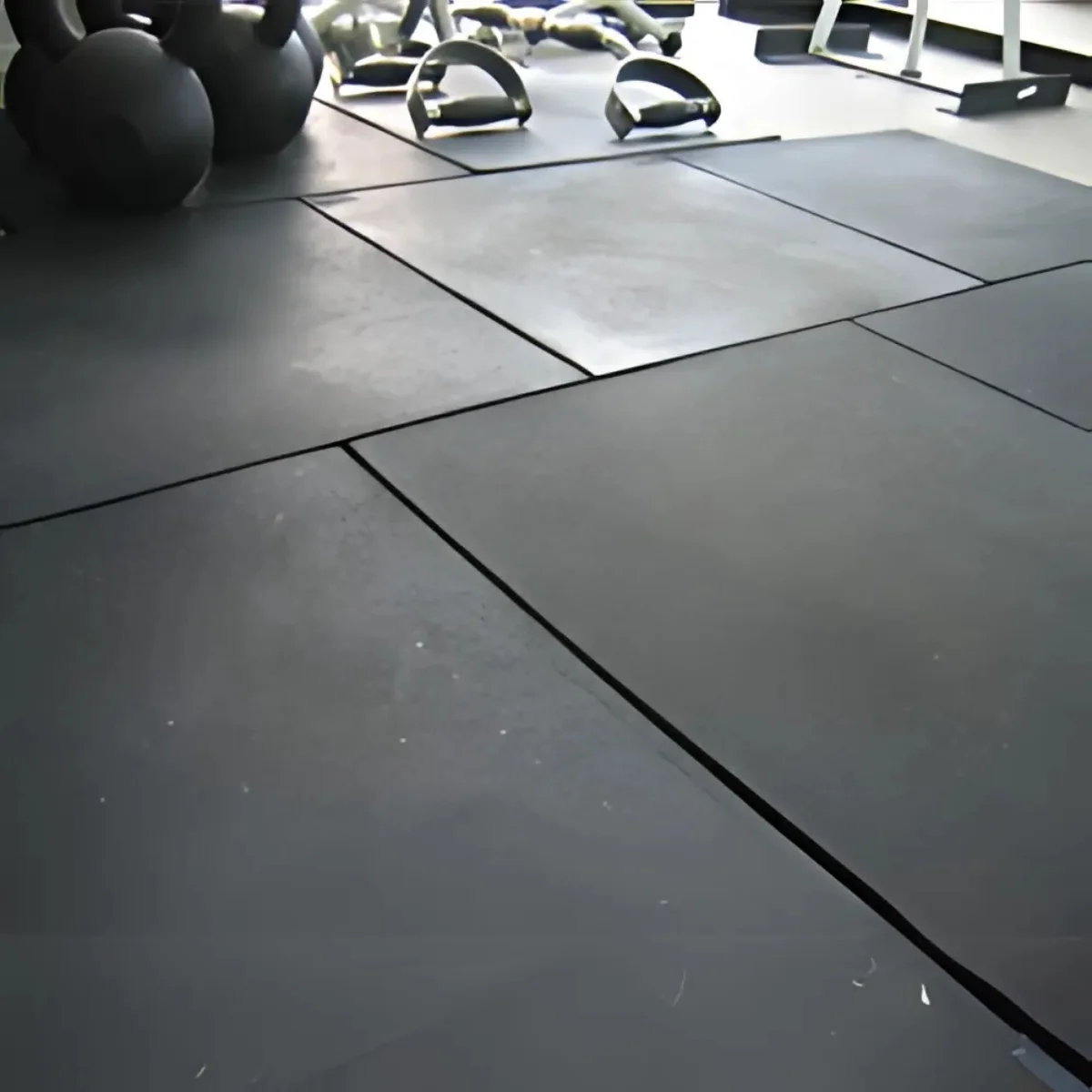 Black rubber gym tiles on the floor. Kettlebells and other equipment are in the background.