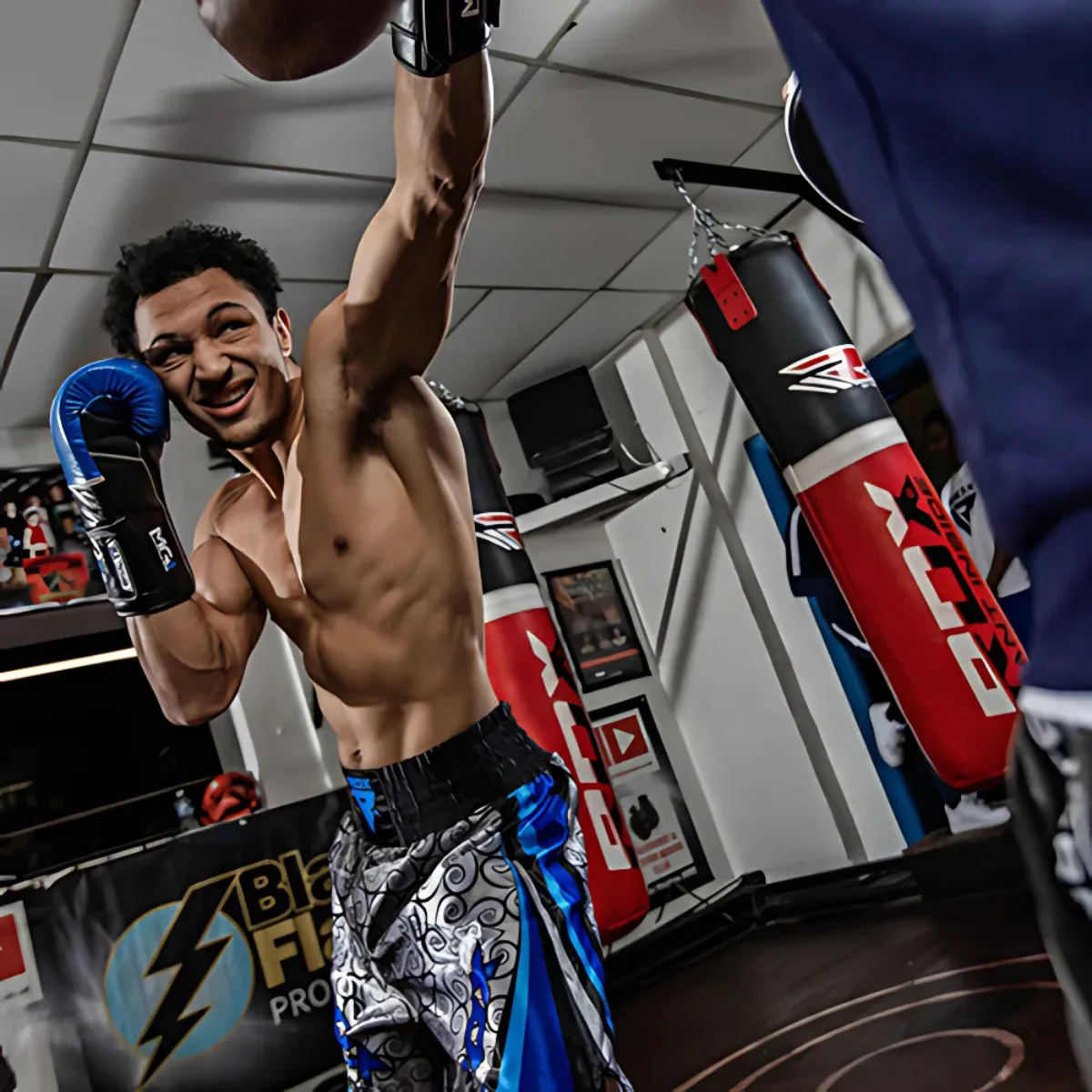 Boxer in the ring throwing a punch. Boxing gloves and red punching bags are in the background.