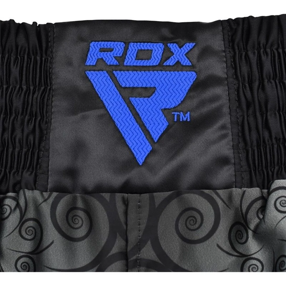 Close-up of black Muay Thai shorts with blue RDX logo. Swirl pattern at the bottom.