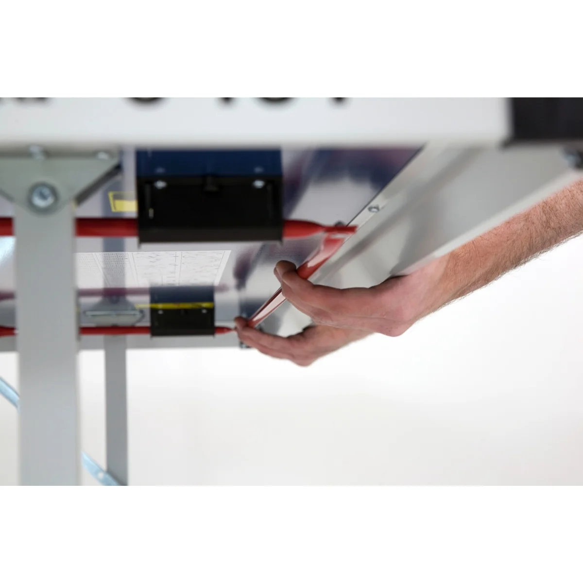 A person's hands are holding a metal sheet or shelf. The person is near a white surface.