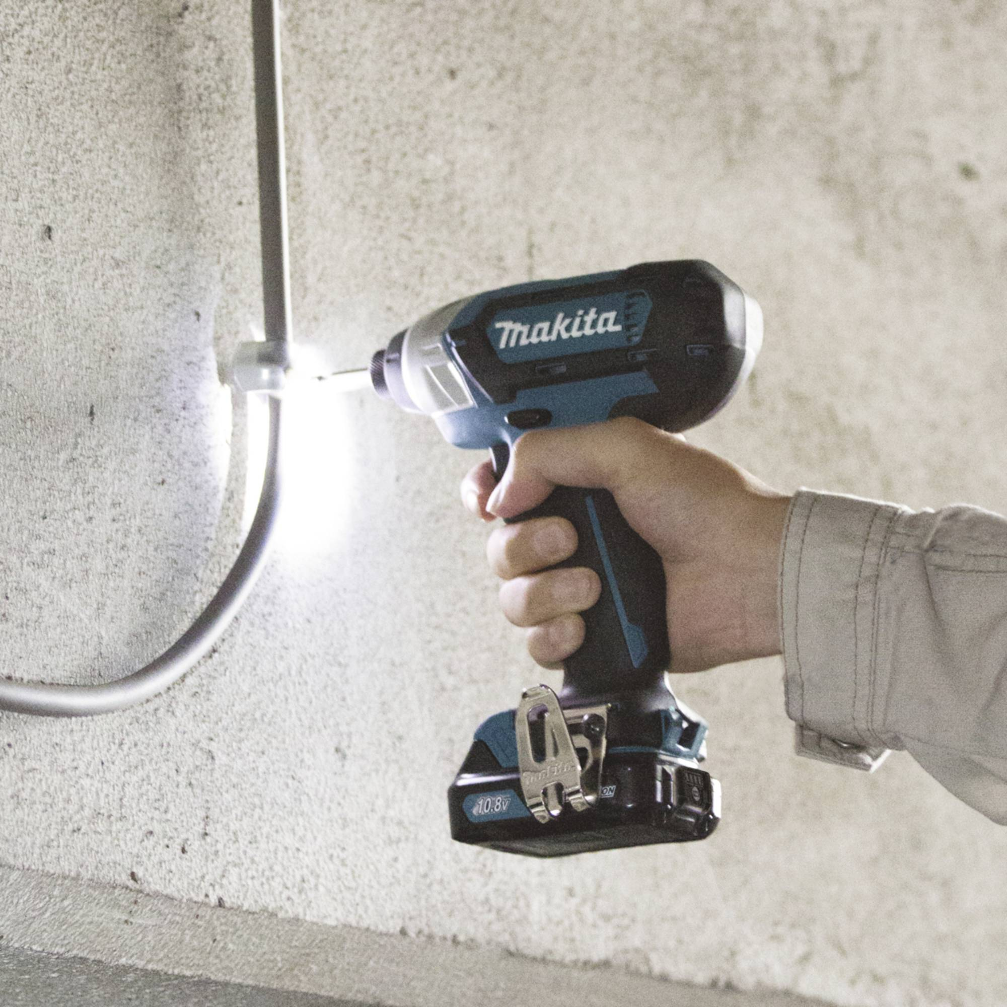 Mano che tiene un trapano Makita, che fora un tubo metallico contro un muro di cemento.