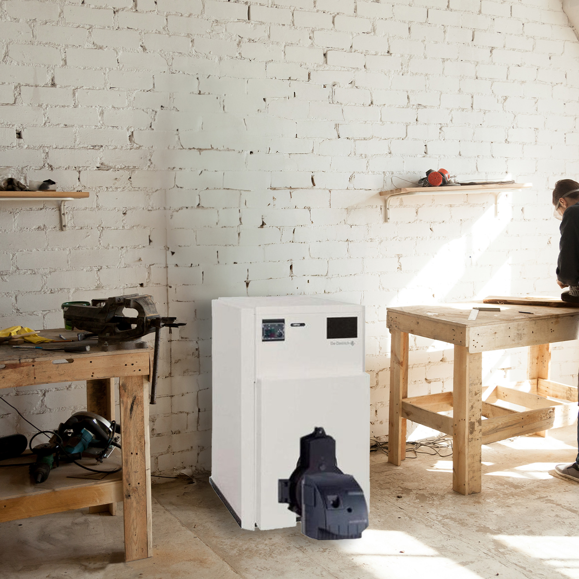 Un taller con una máquina blanca, mesas de madera y una pared de ladrillos. Dos personas trabajando.