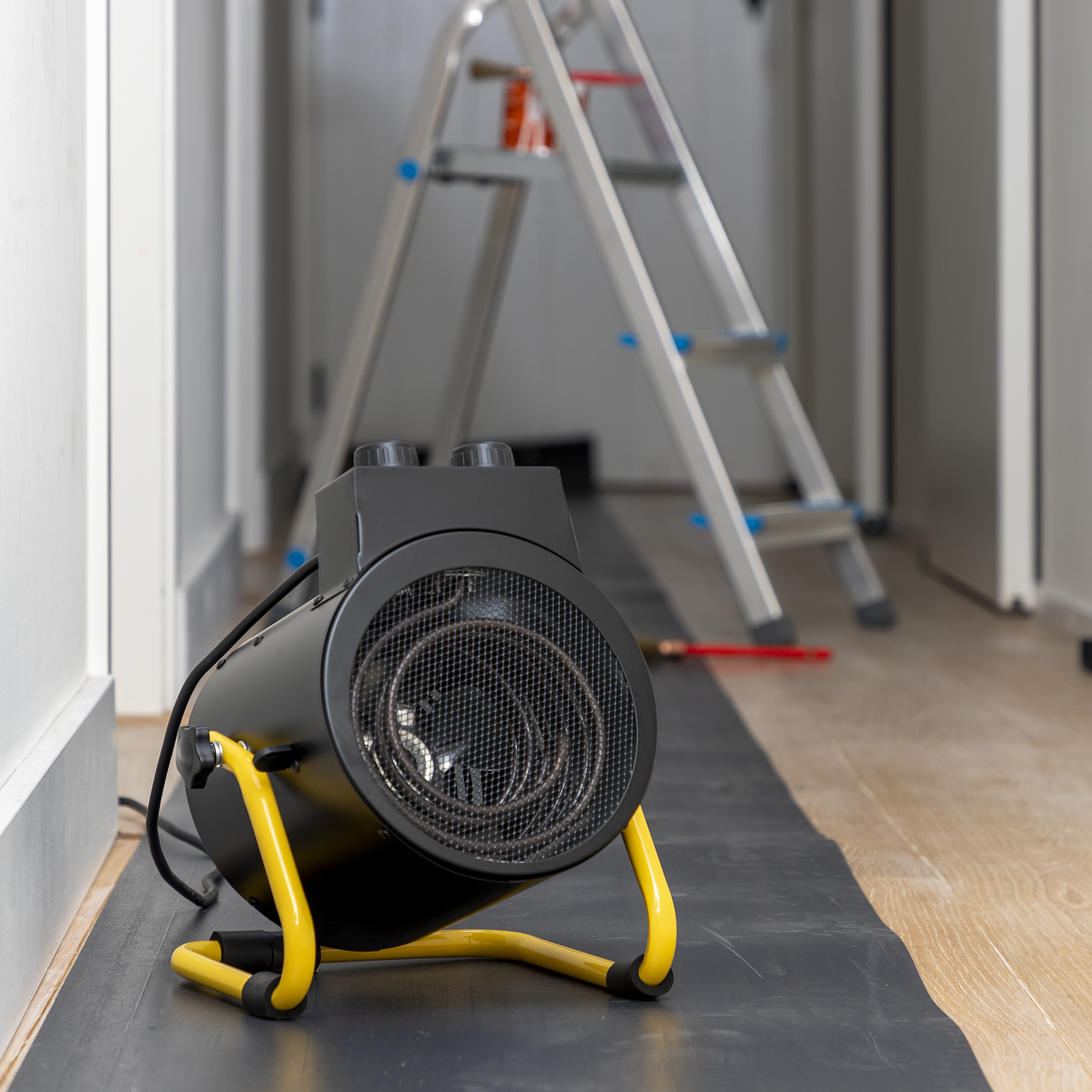 Een zwart-gele elektrische kachel in een kamer met een ladder en een zwart mat.