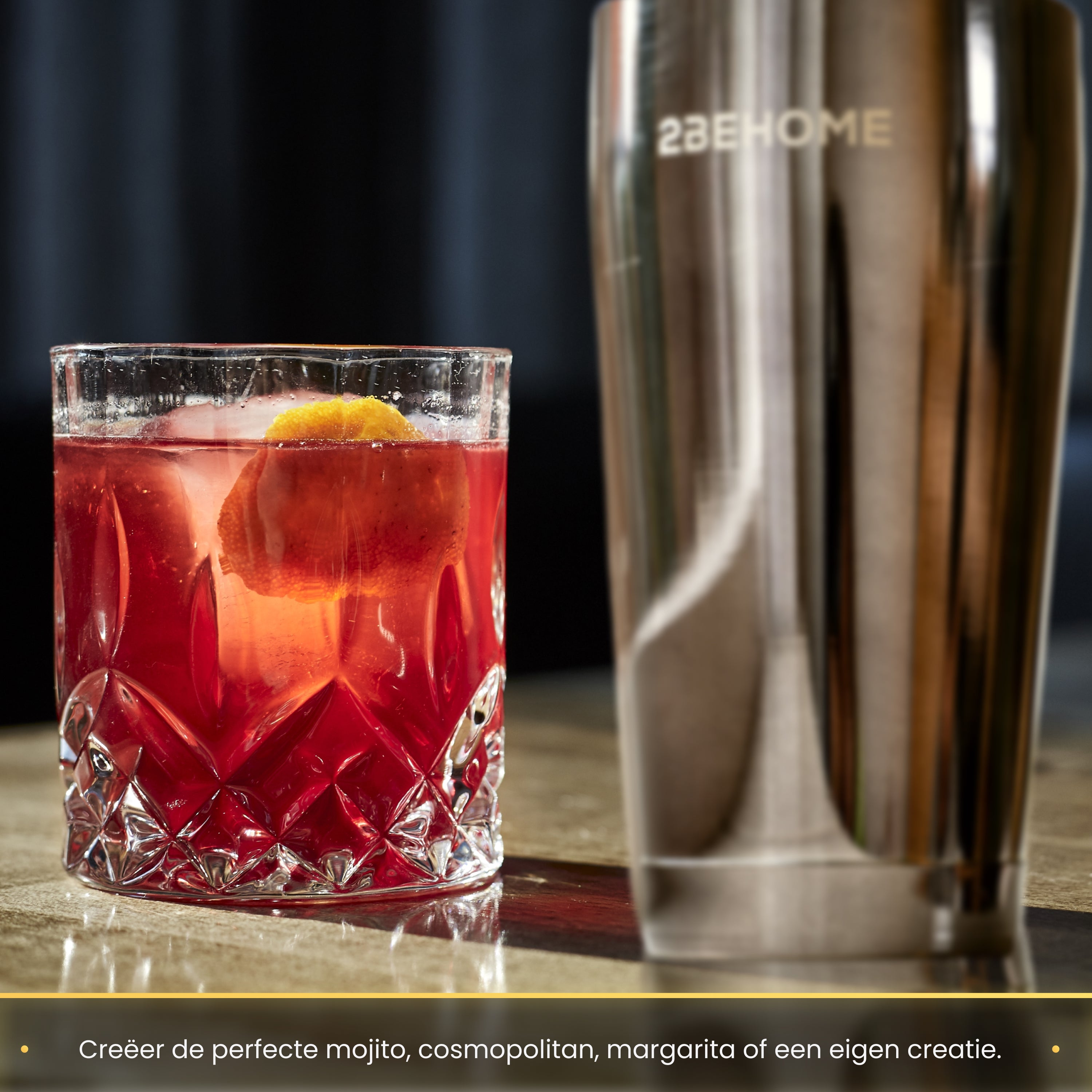 A cocktail in a glass with an orange slice, next to a silver shaker.