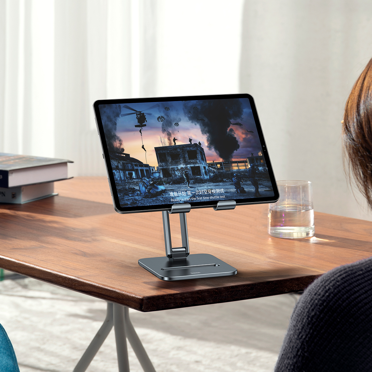 Tablet na stojaku wyświetlający scenę wojenną. Kobieta patrzy na tablet.