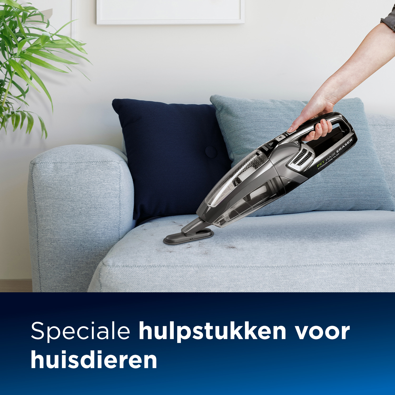 Hand benutzt einen schwarz-silbernen kabellosen Staubsauger auf einem hellblauen Sofa. Dunkelblaues Kissen im Hintergrund.