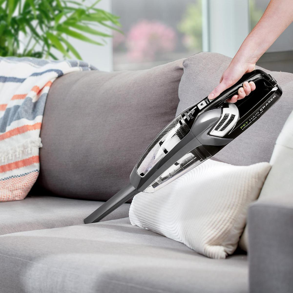 Ein Handstaubsauger, der ein Sofa mit einem schwarz-grauen Staubsauger absaugt.