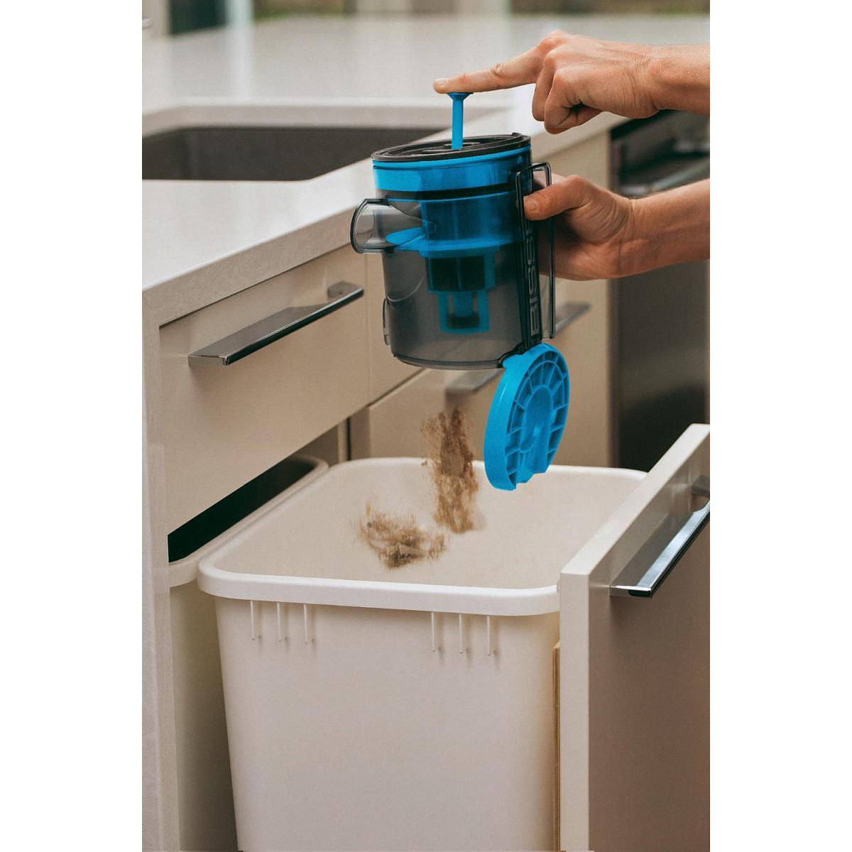 Ręka trzymająca niebiesko-czarny odkurzacz, opróżniająca zanieczyszczenia do kosza.