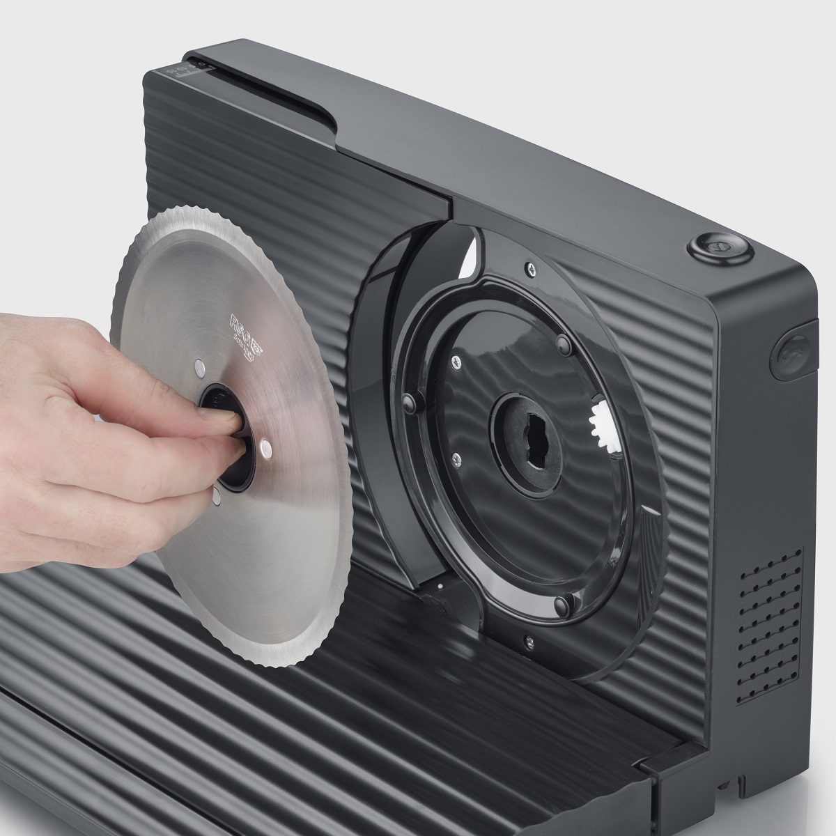 Osoba wymienia okrągłe ostrze w czarnej krajalnicy do żywności. Ostrze jest srebrne.