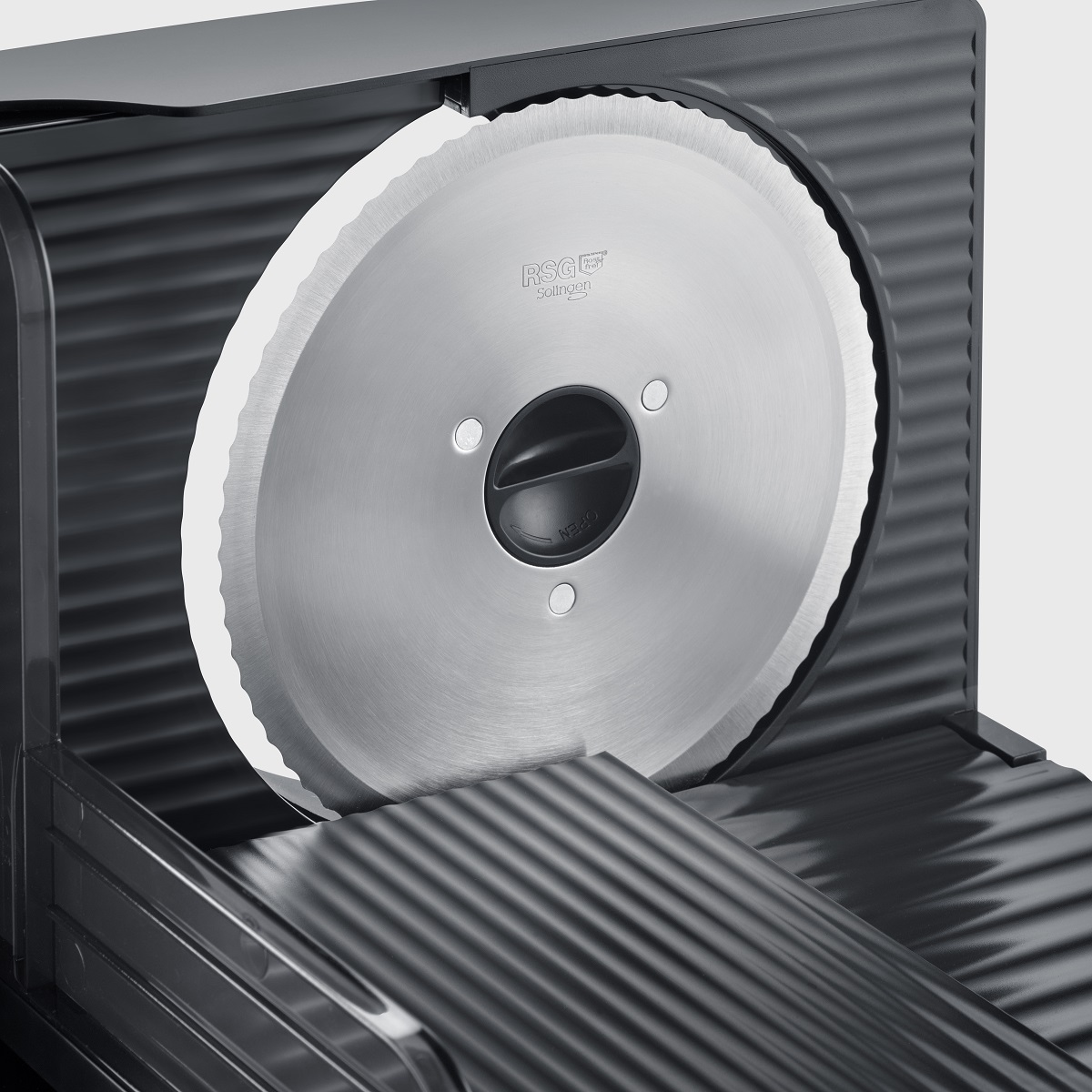 Krajalnica do mięsa z dużym, okrągłym ostrzem. Maszyna jest ciemna, ze srebrnym ostrzem.