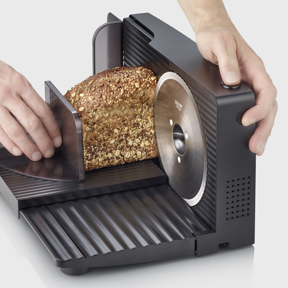 Krojalnica do chleba z bochenkiem chleba w trakcie krojenia, zbliżenie na ostrze.