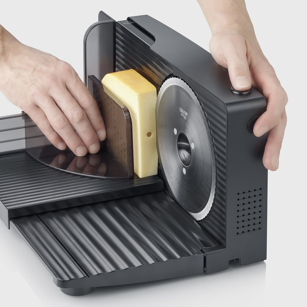 Ręce krojące blok sera czarną krajalnicą. Obecny jest plaster sera. Białe tło.