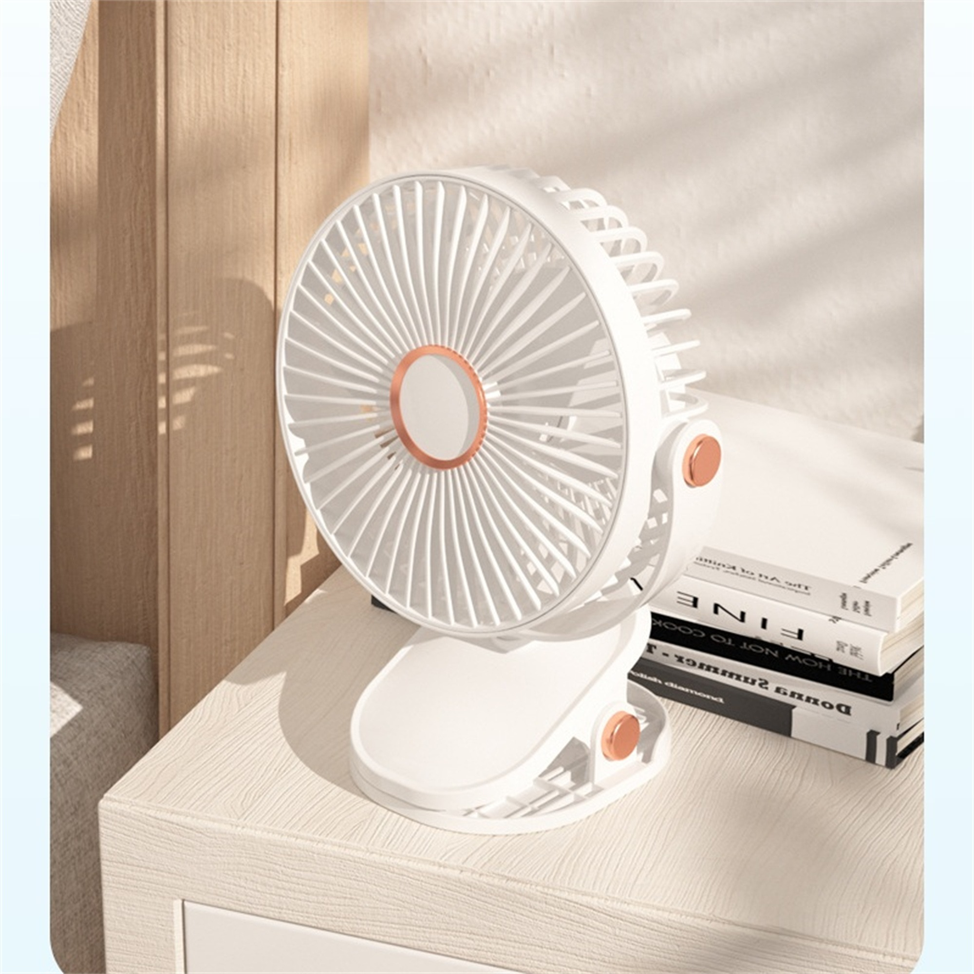 Weißer und roségoldener Ventilator auf einem Schreibtisch. Bücher sind im Hintergrund.