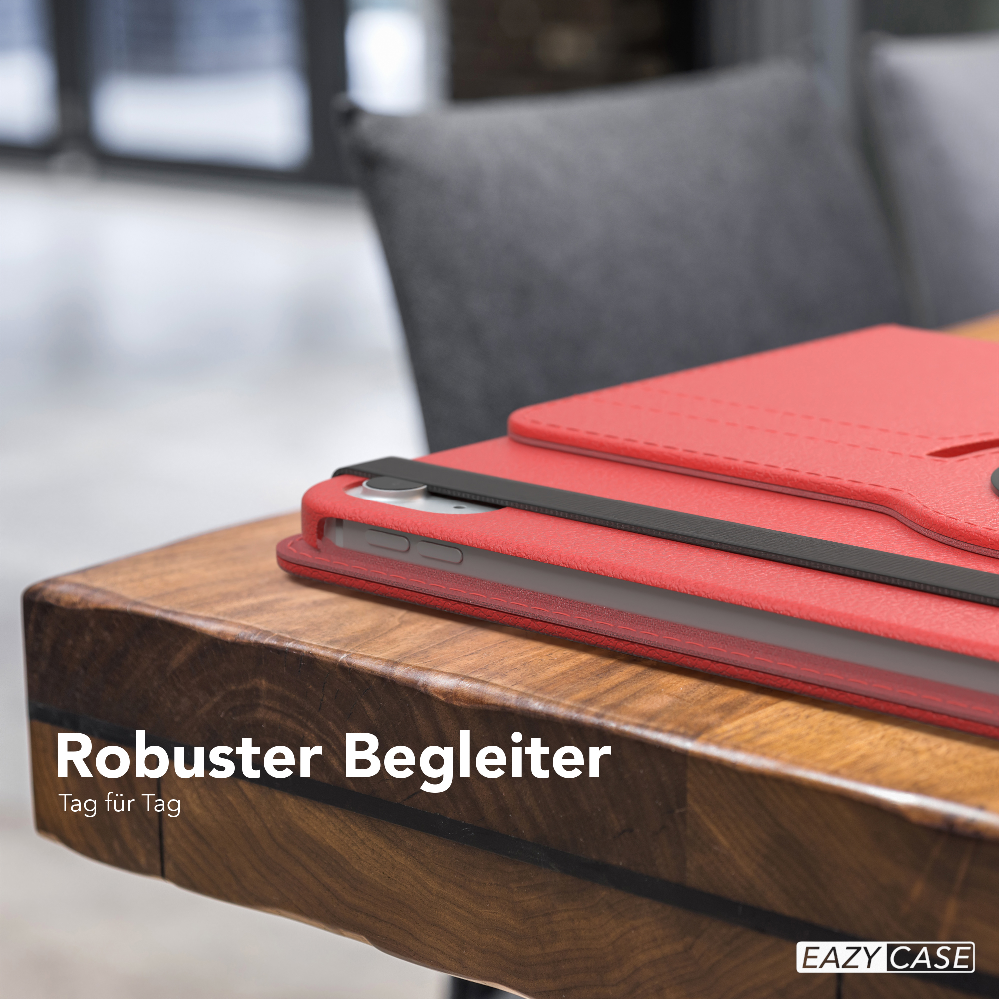 Rote Tablethülle auf einem Holztisch, mit einem Tablet darin, vor einem grauen Stuhl.