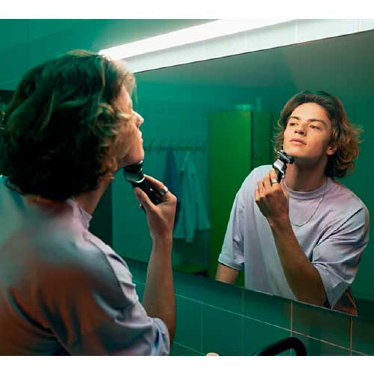 Mężczyzna goli się w lustrze. Odbija się, goląc policzek czarno-srebrną golarką.