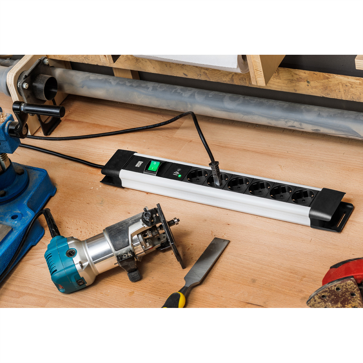Steckdosenleiste mit mehreren Steckdosen. Ein blauer Router und andere Werkzeuge auf einem Holztisch.