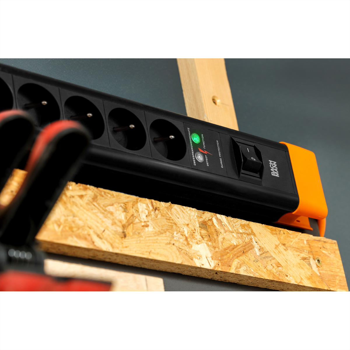 Schwarze Steckdosenleiste mit orangen Enden. Holz- und grauer Hintergrund.