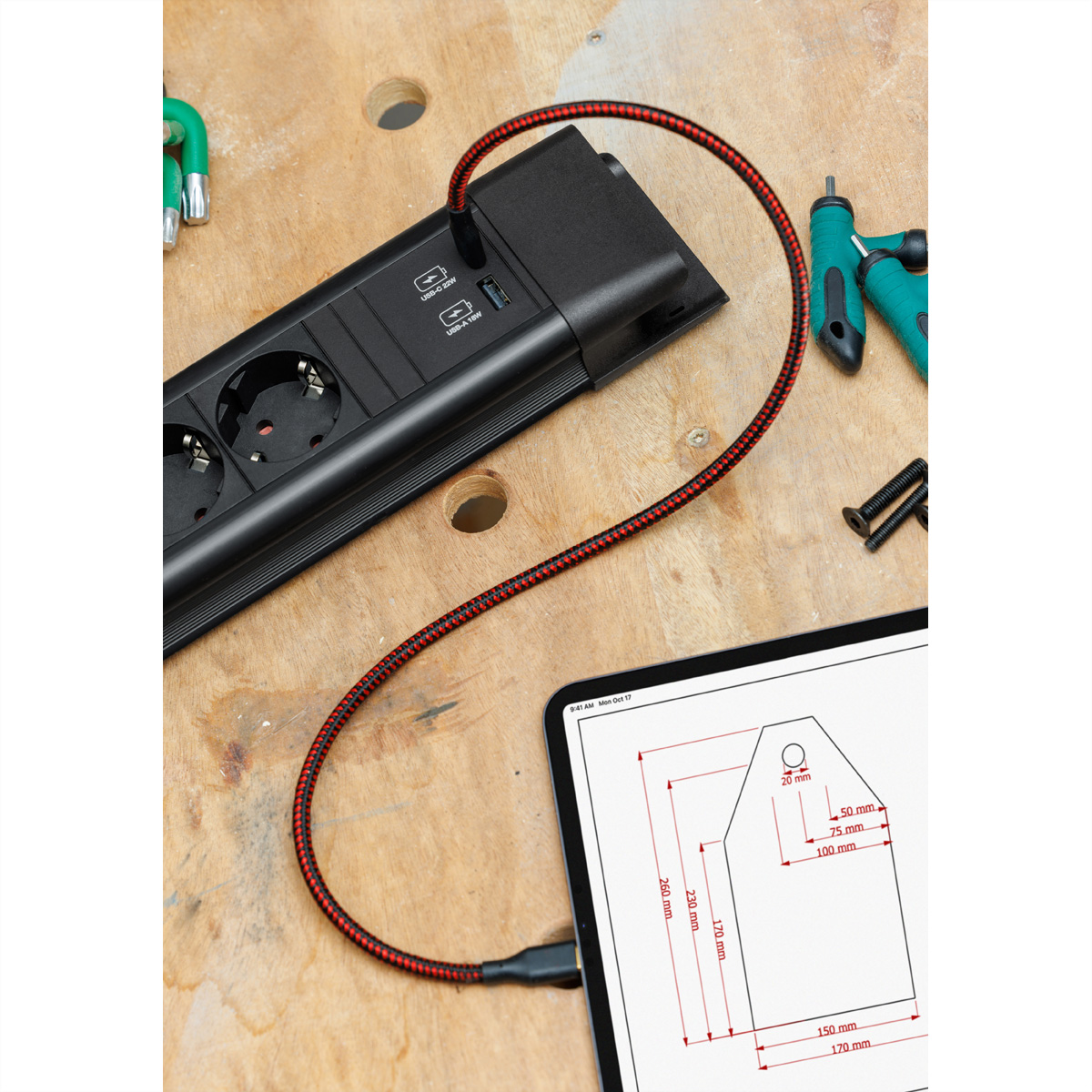 Eine schwarze Steckdosenleiste mit rotem Kabel und ein Tablet mit einer Zeichnung auf Holz.