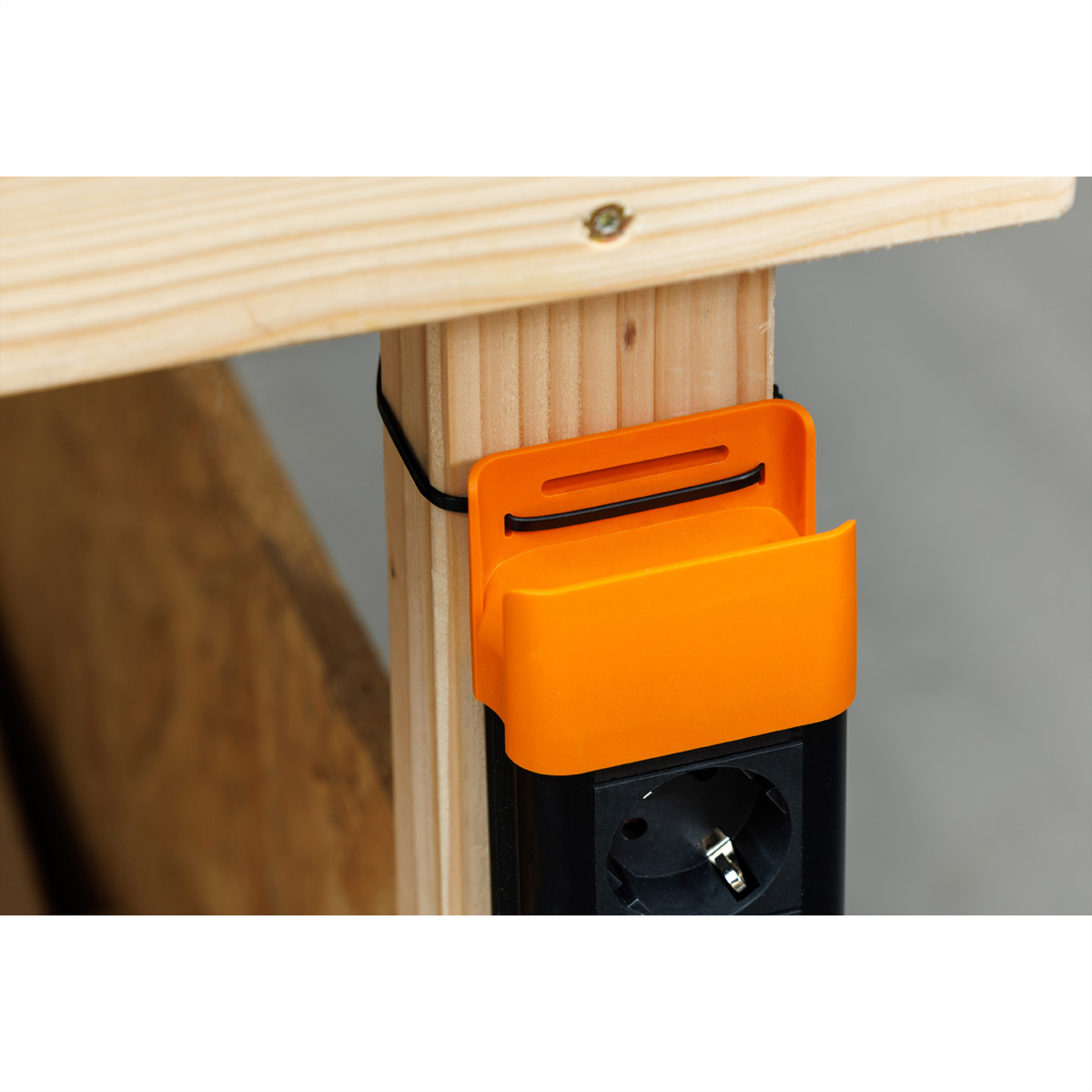 Ein orangefarbener Steckdosenhalter an einem Holzbalken mit einer schwarzen Steckdose und Kabel.