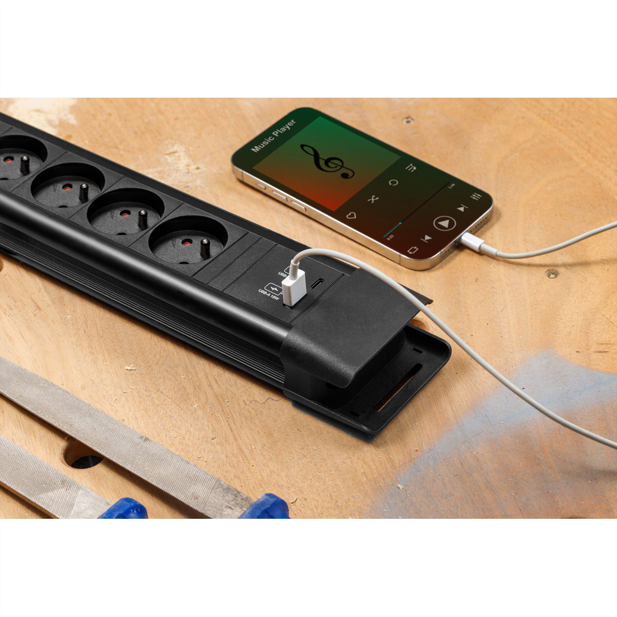 Zwarte stekkerdoos met stopcontacten en een telefoon die oplaadt. Telefoon toont muziekspeler interface. Hout.