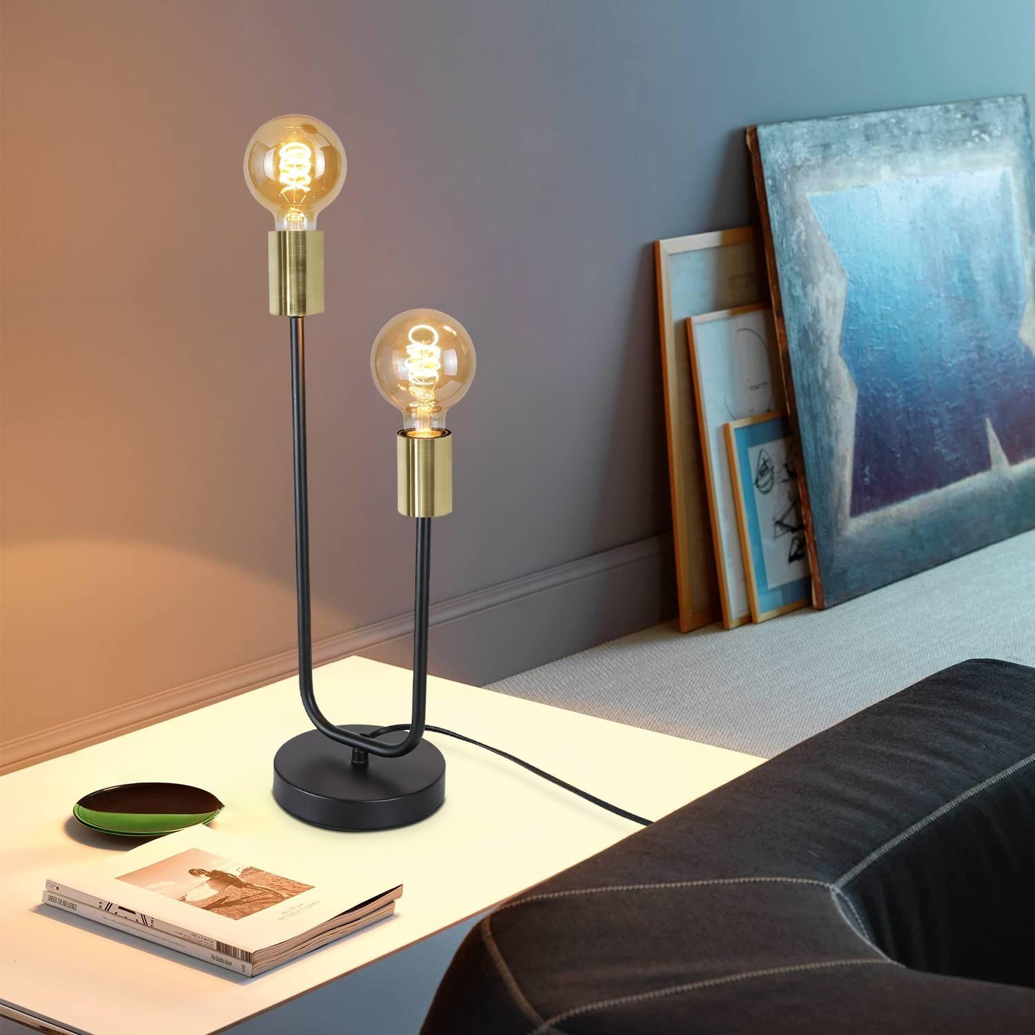 Czarna lampa z dwiema żarówkami, umieszczona na białej powierzchni. Sztuka w tle.