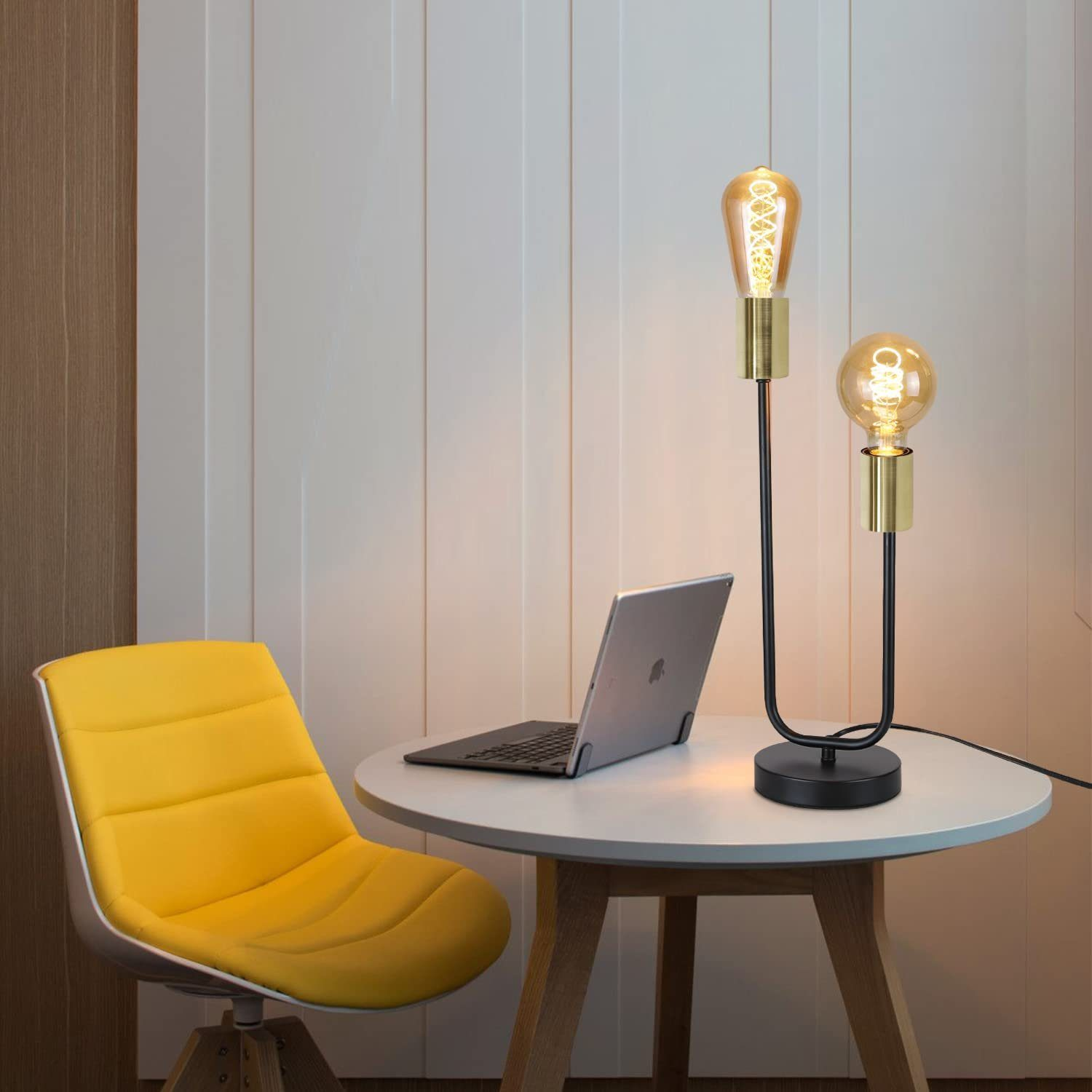 Ein Tisch mit zwei Lampen mit Edison-Glühbirnen, einem Laptop und einem gelben Stuhl vor einer weißen Wand.