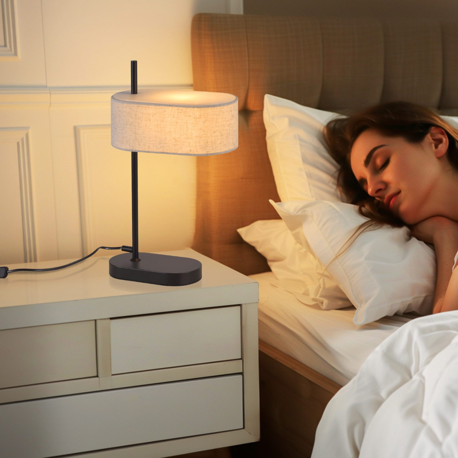 Kobieta śpi obok lampy stołowej. Lampa ma abażur z tkaniny i czarną podstawę.