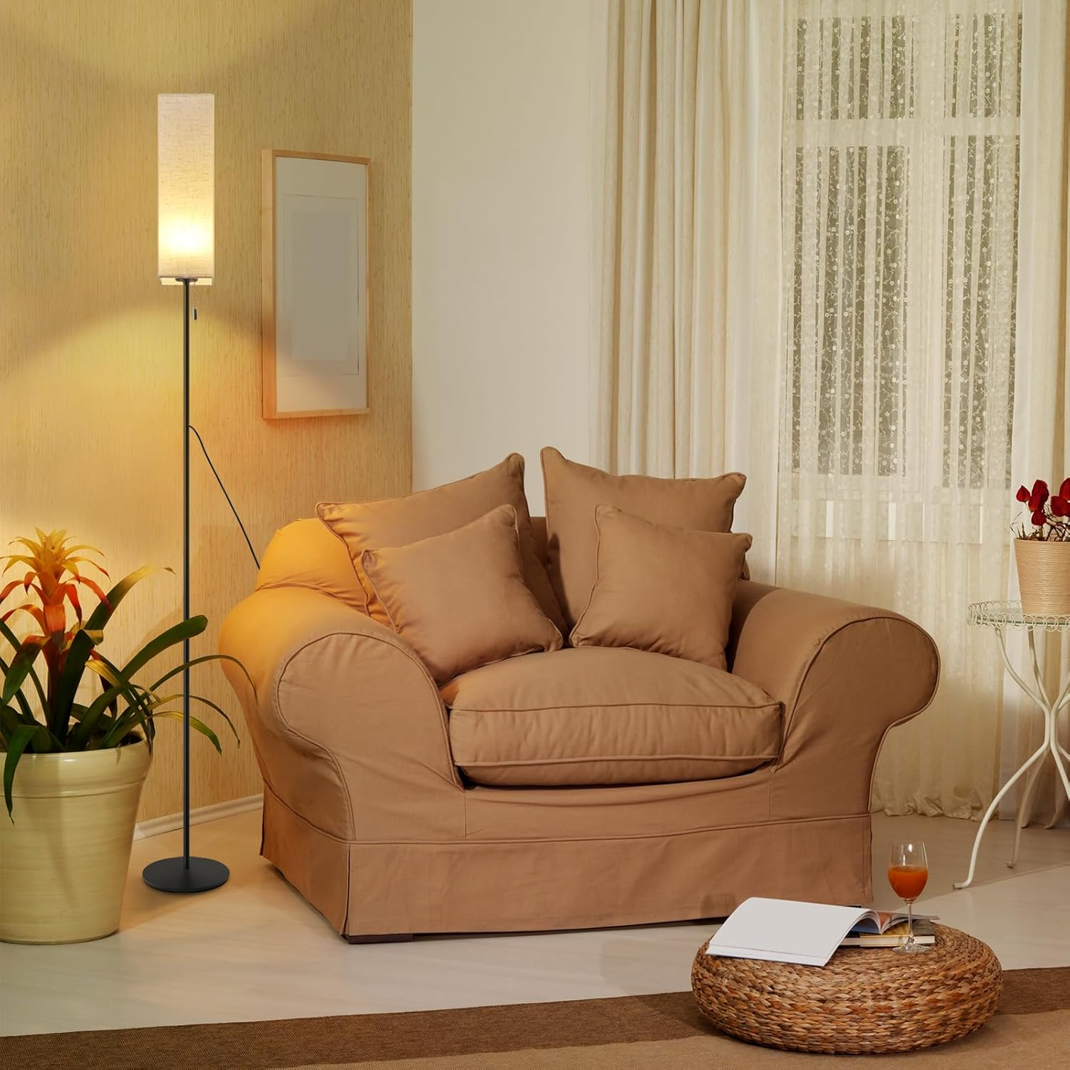 Beżowy fotel z poduszkami obok lampy podłogowej i rośliny doniczkowej. Stół z napojem i książką.