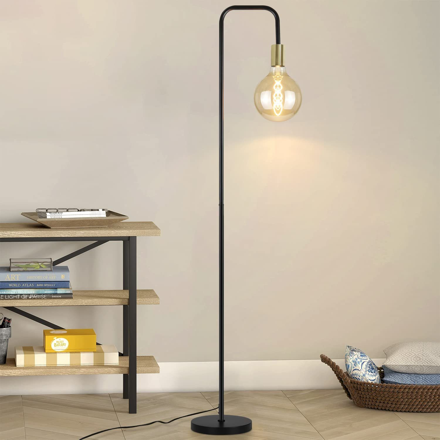 Una lampada da terra nera e oro con una grande lampadina, accanto a una libreria e un cestino.