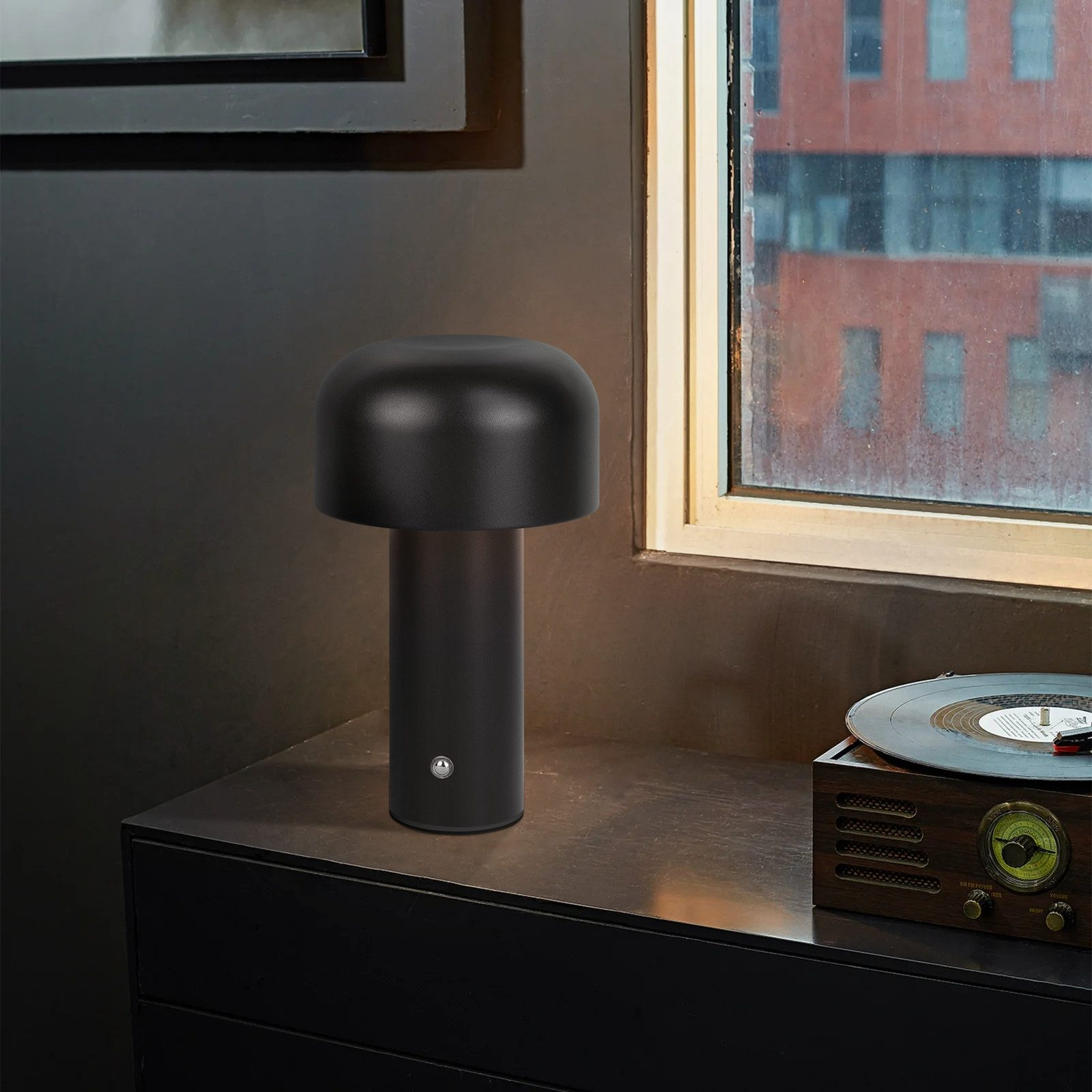 Czarna lampa na ciemnej powierzchni obok okna i gramofonu.