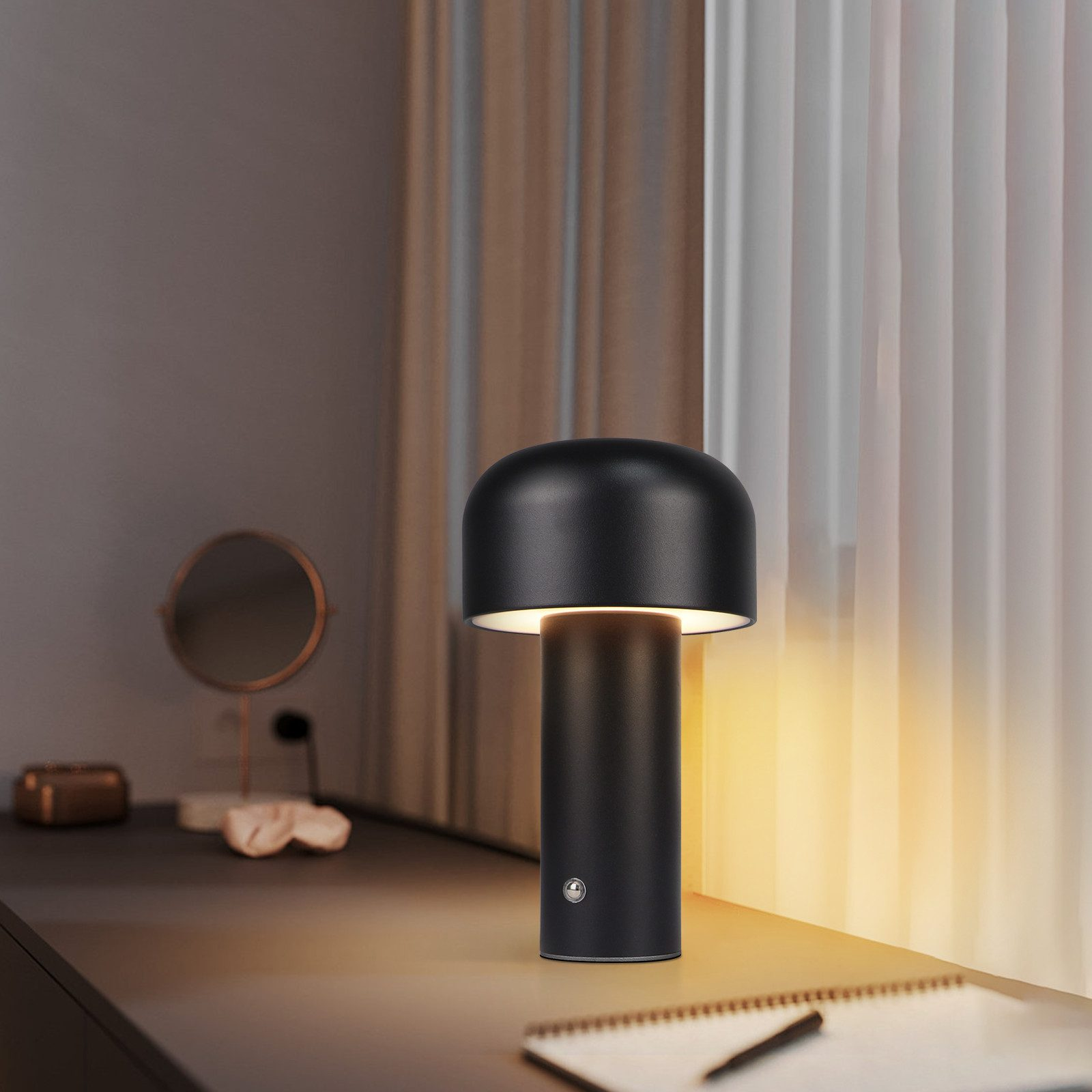 Czarna lampa na biurku z lustrem i notatnikiem w tle.